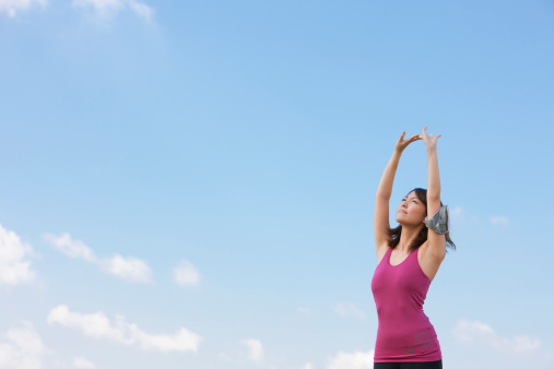 Woman with brown hair and a pink top stretching up in front of the sky