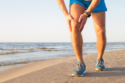 Man running on the beach holding his knee in pain