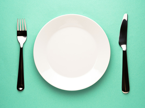 An empty plate in-between a knife and fork on a blue background