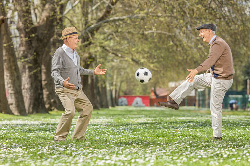 Two elderly men playing football in a park