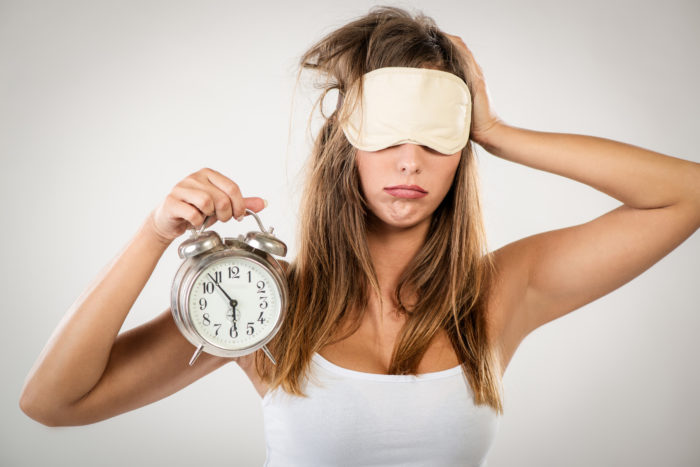 A woman holding an alarm clock and wearing a sleep mask