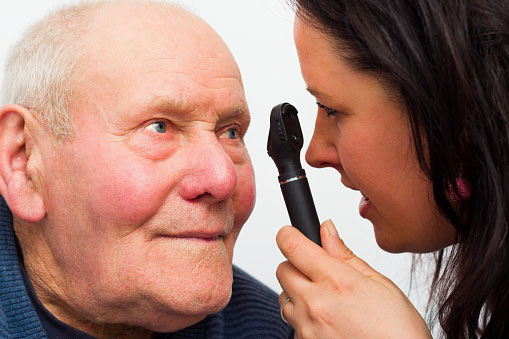 A woman looking into an elderly mans eye using a tool