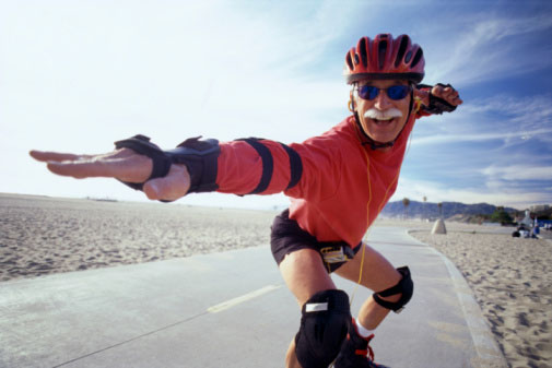 Elderly man rollerblading next to a beach wearing protective gear