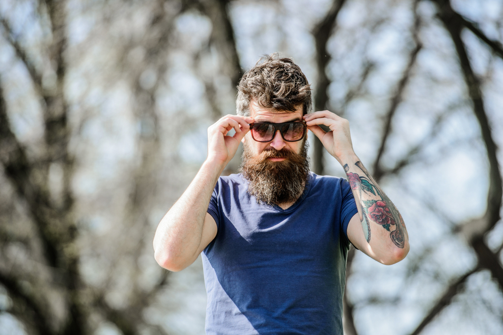 Man with blue t-shirt and large beard putting sunglasses on