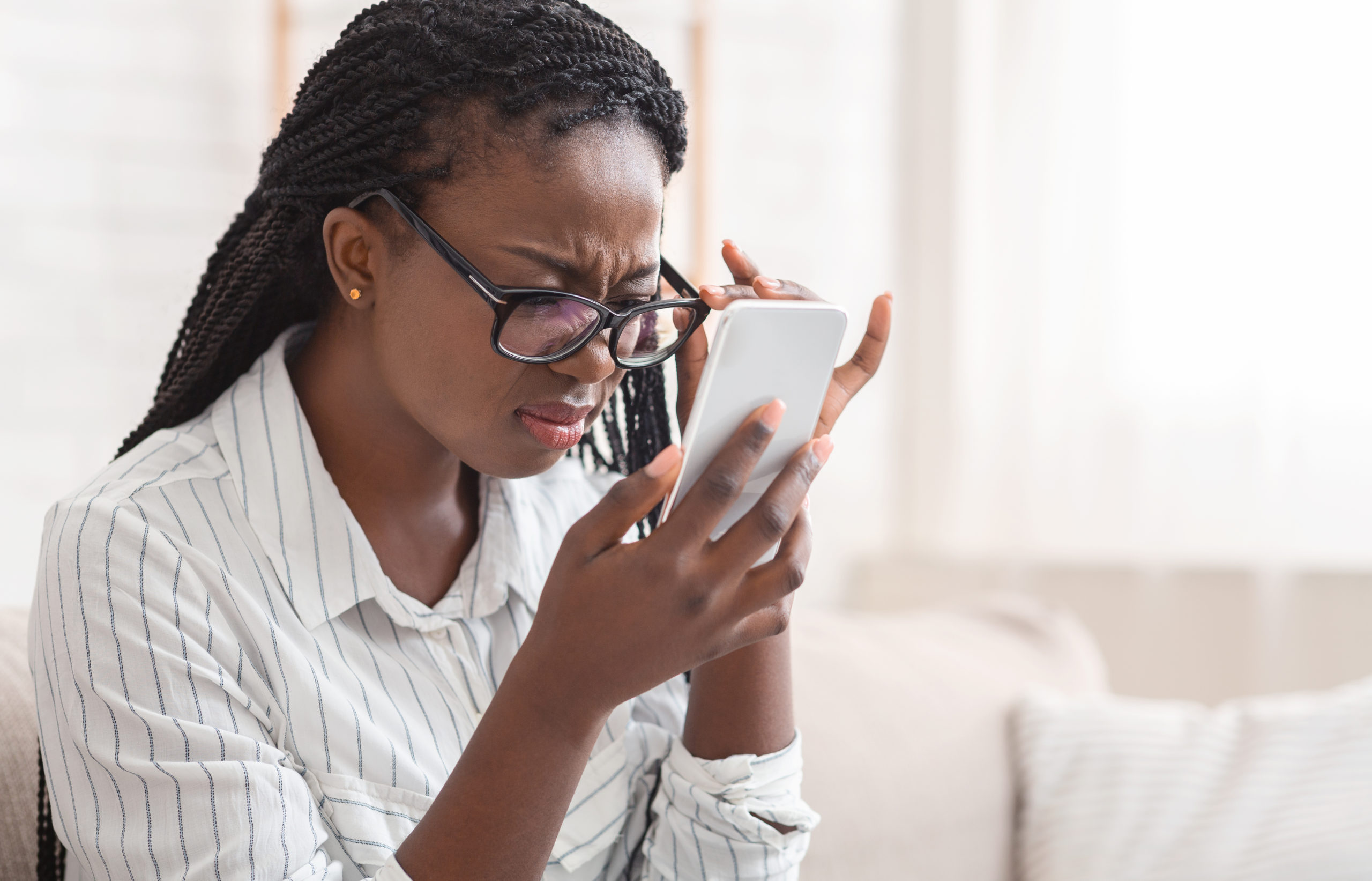 Woman squinting at her phone whilst readjusting her glasses