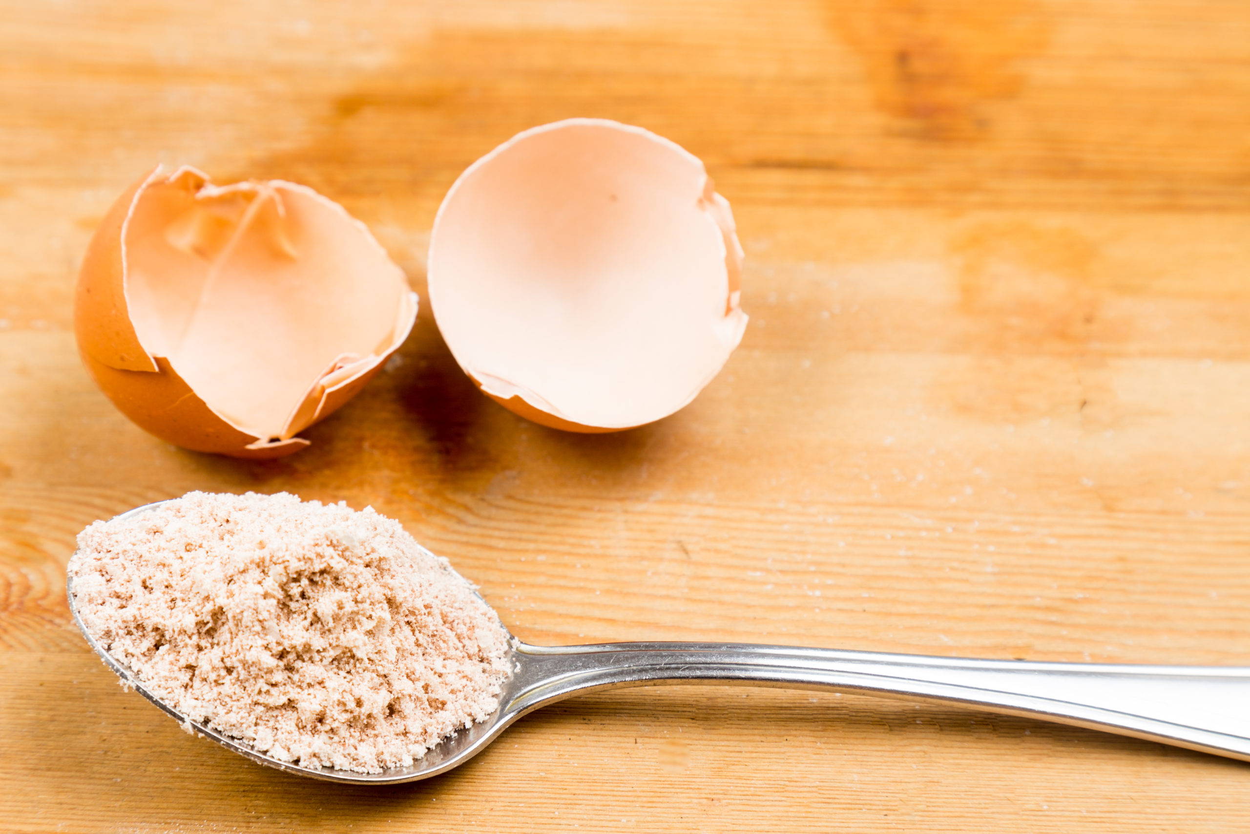 A heaped spoon of sand and an empty cracked egg on a table