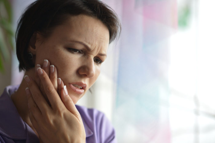 A woman with dark brown short hair holding her cheek because of tooth pain