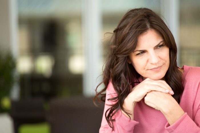 A woman with brown hair and a pink top deep in thought