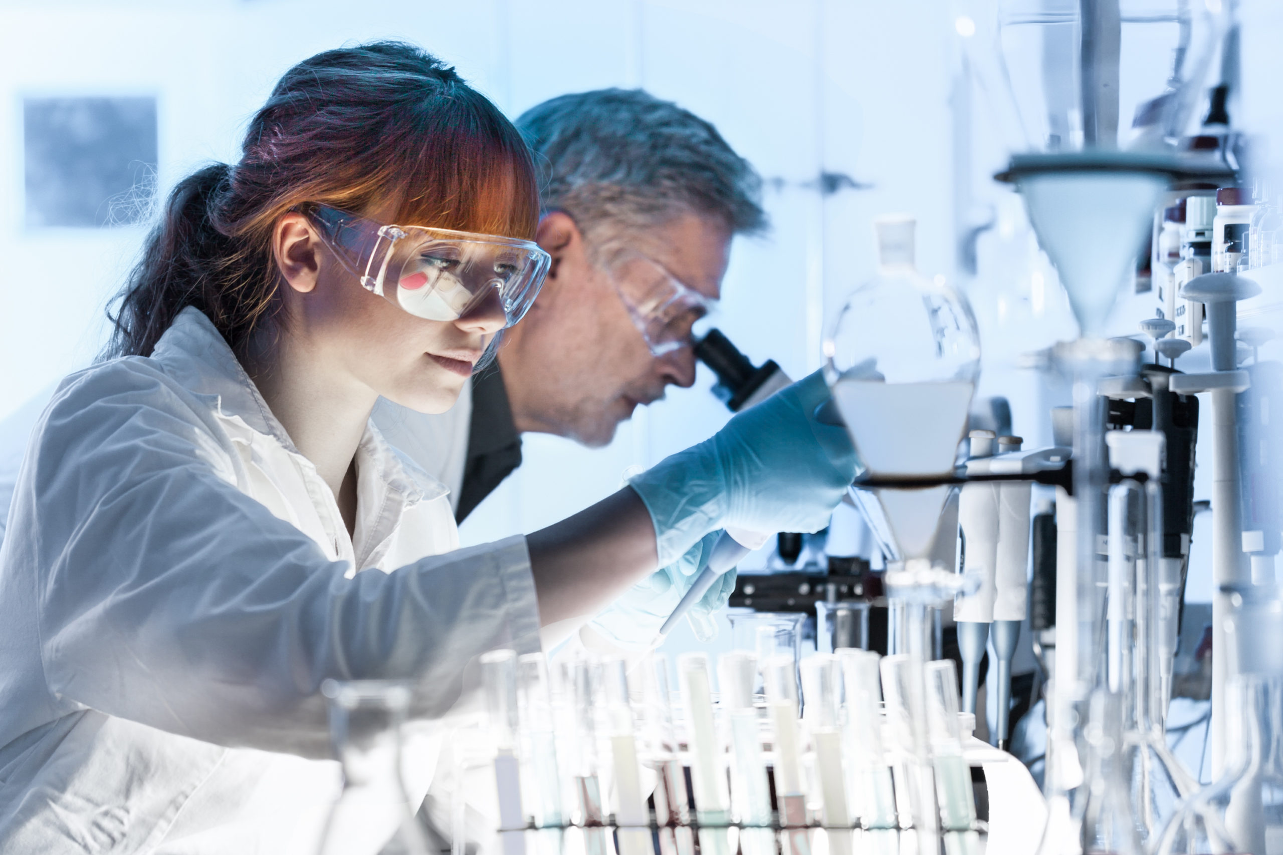 Woman and man wearing lab coats using microscopes in a lab