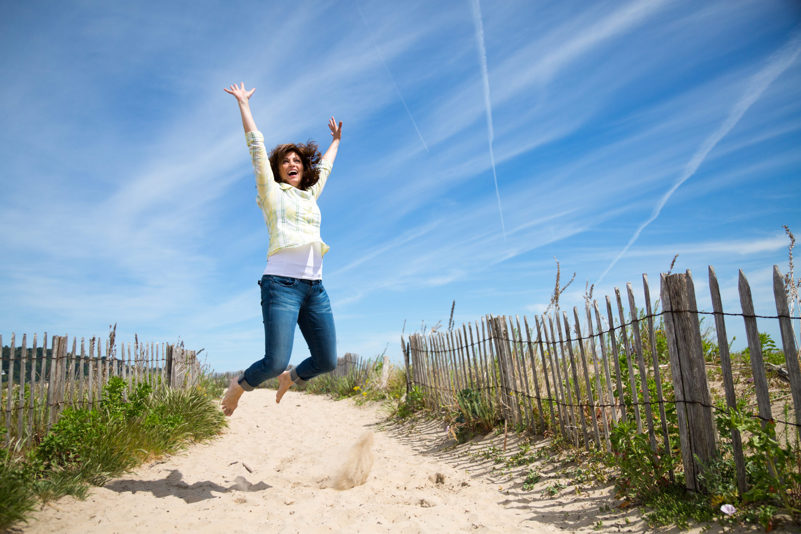 Woman jumping on a sandy beach wearing a yellow shirt and jeans