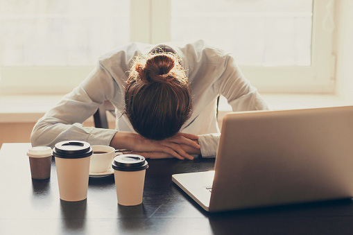 Woman falling asleep in front of her computer surrounded by coffee